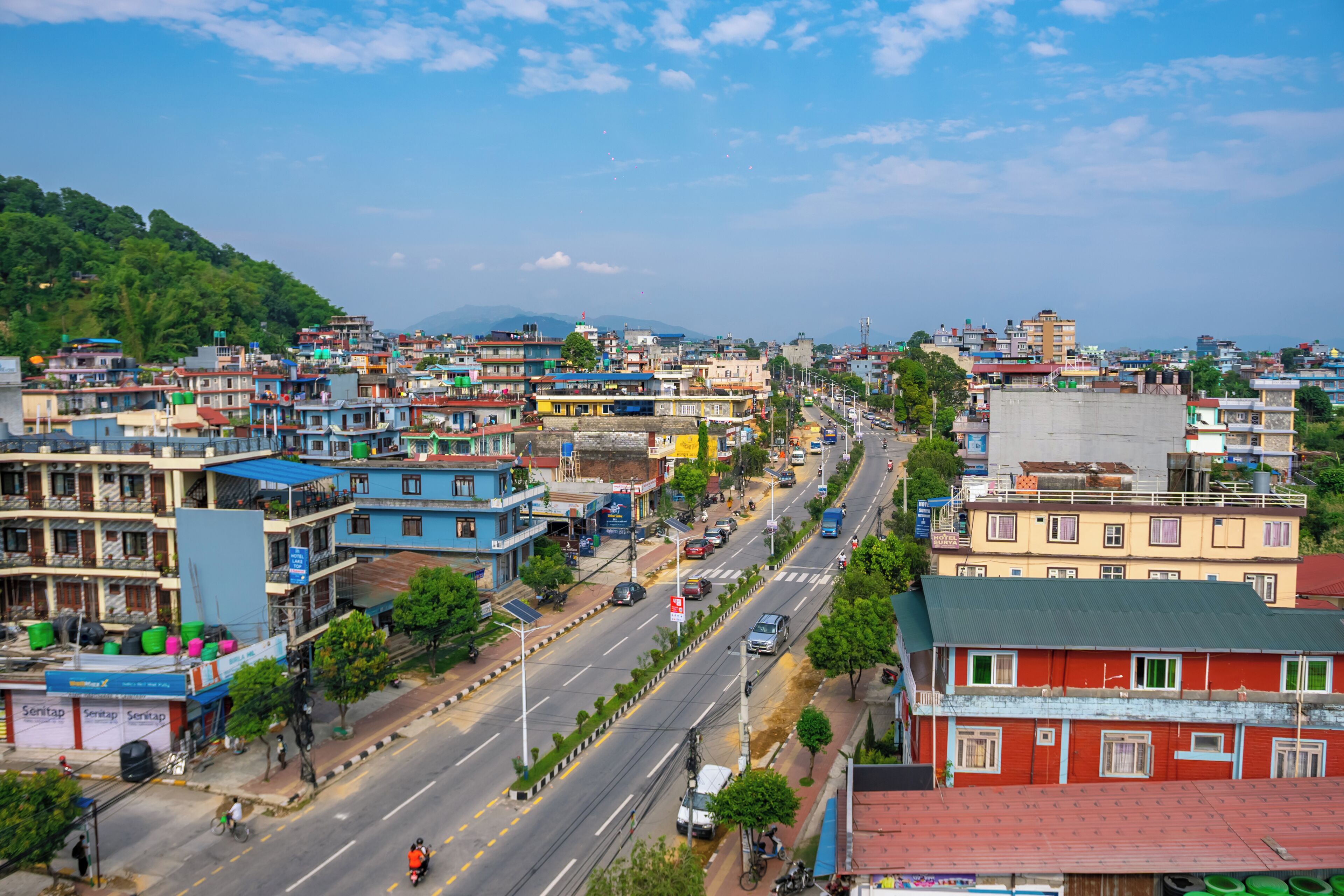 A cityscape with a wide street, buildings, and greenery.