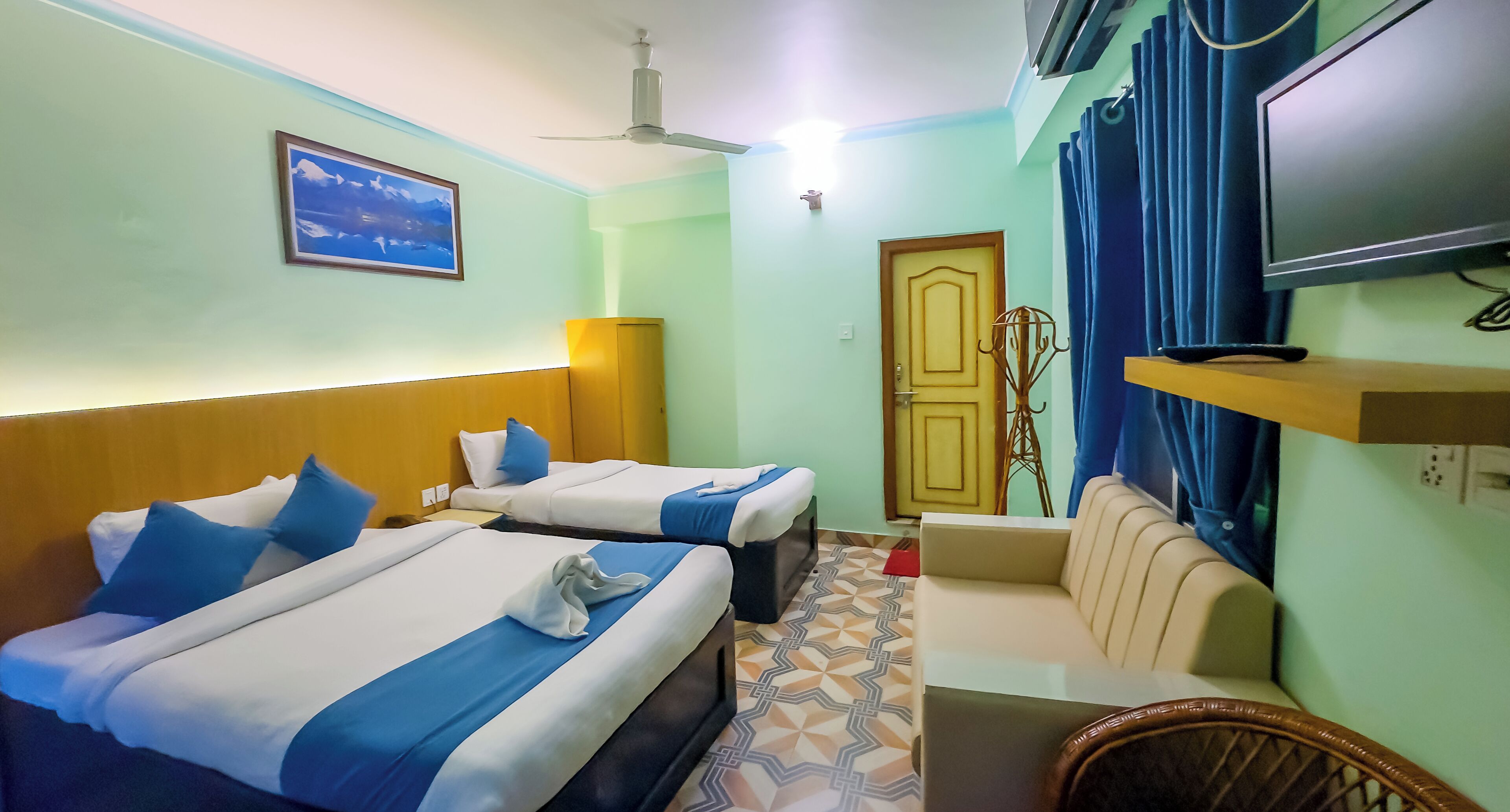 A hotel room with two beds, a sofa, a TV, and a ceiling fan.