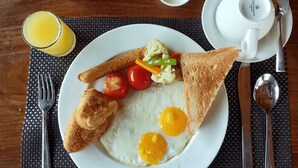 A breakfast plate with eggs, toast, and vegetables, accompanied by a glass of orange juice, a teapot, cups, and cutlery on a wooden table. - Hotel Rudrakshya Pokhara (Pokhara)