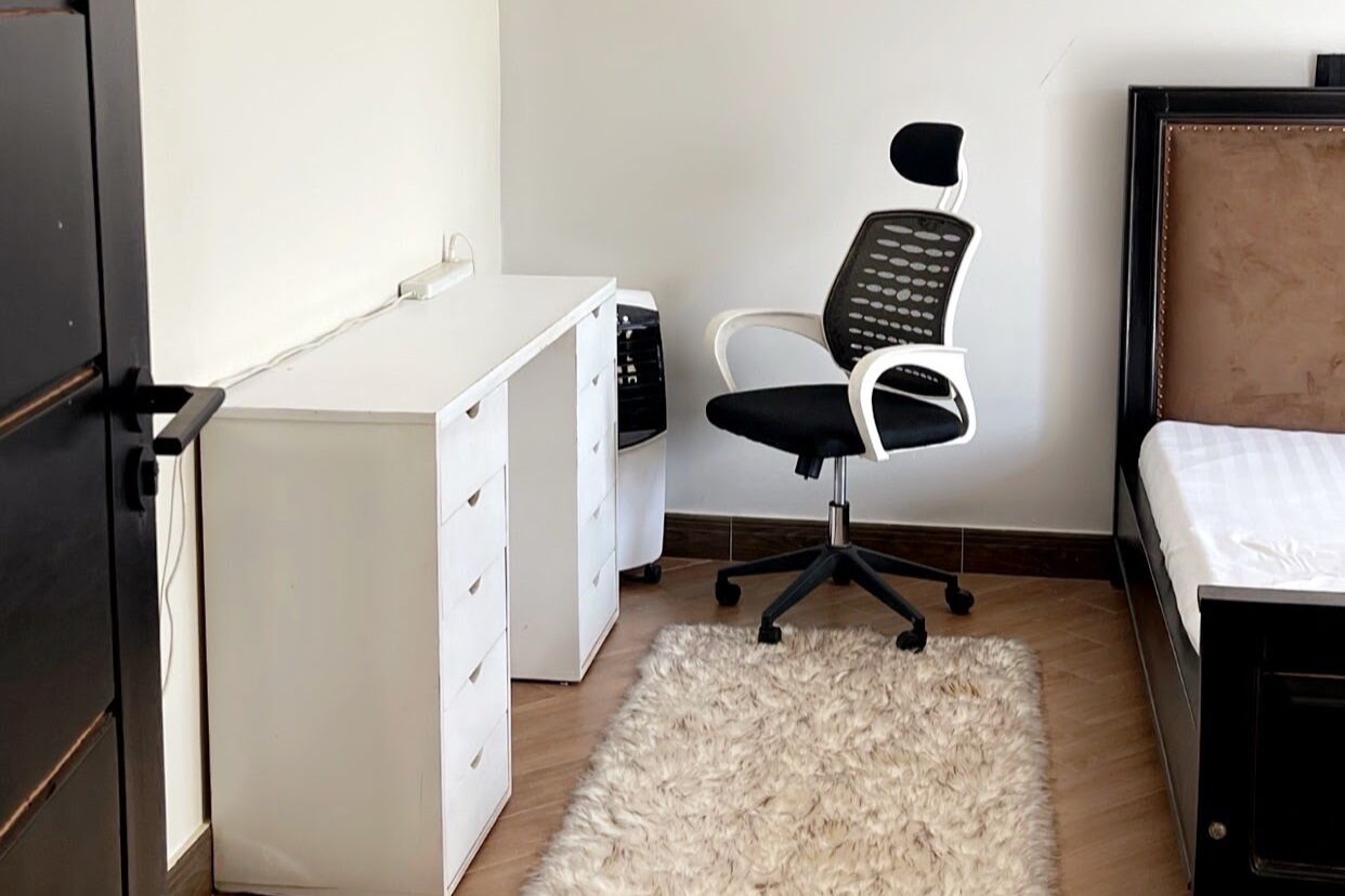 Un dormitorio con cama, escritorio con cajones, una silla y una alfombra mullida.