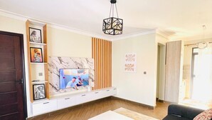 Una sala de estar moderna con un mueble blanco para el equipo de entretenimiento, sofás negros, una mesa de centro blanca y una pared de acento de madera.