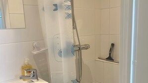 Une salle de bain avec une douche, un lavabo équipé d’un distributeur de savon et un miroir.
