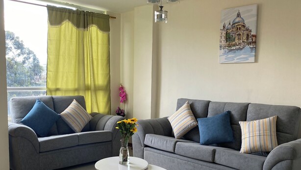 A living room with two grey sofas, a white coffee table, and a painting of a building on the wall.