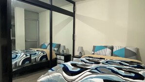 A modern bedroom with a large bed, a wardrobe with a mirror, and a ceiling light.