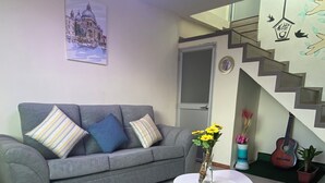 A living room with a grey sofa, a round white table, and a staircase with a railing.