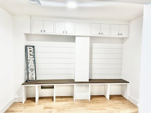 Een kamer met witte paneelwanden, een donkerhouten bankje en witte kasten met zwarte handgrepen.