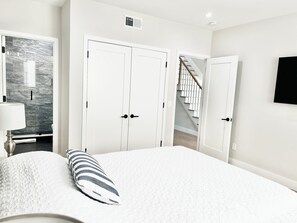 A bedroom with a bed, a nightstand, a lamp, a wardrobe, and a staircase leading to another floor. - 1 Block To The Beach -NEW House (Manasquan)