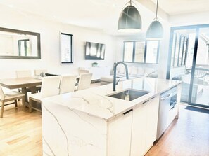 A modern kitchen with a marble island, a dining area with a wooden table and chairs, and a large window providing natural light. - 1 Block To The Beach -NEW House (Manasquan)