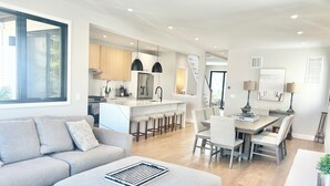 A modern living room with a sofa, ottoman, and a dining area with a table and chairs.