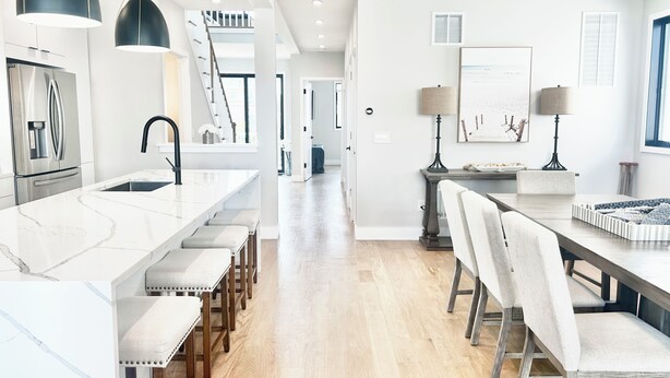 A modern kitchen with a central island, stainless steel appliances, pendant lighting, and a staircase leading to an upper level.