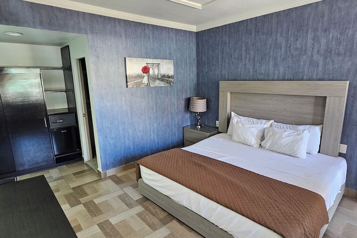 Una habitación de hotel con cama, mesita de noche, lámpara, un cuadro y un armario.