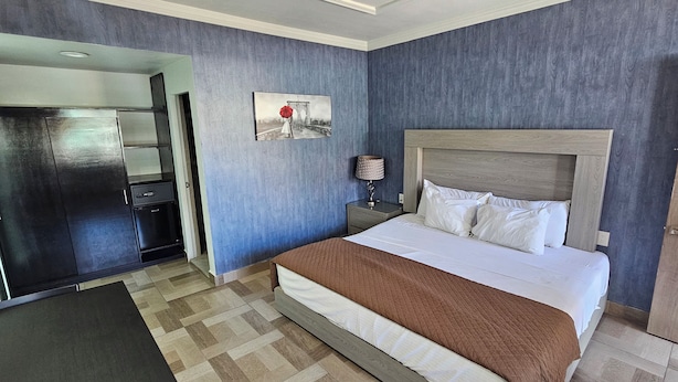 Una habitación de hotel con cama, mesita de noche, lámpara, un cuadro y un armario.