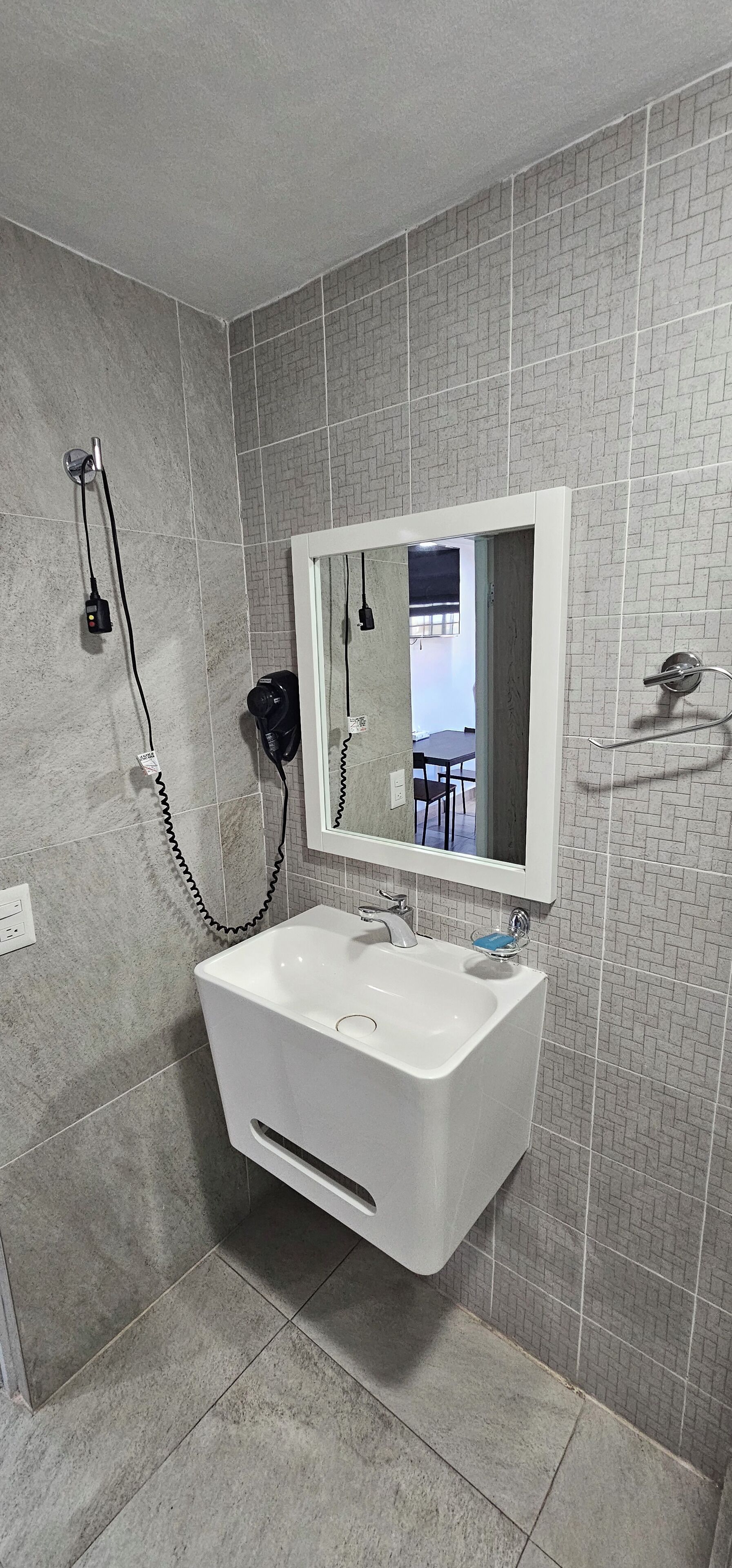 Un baño con un lavamanos blanco, un espejo y un secador de pelo en la pared.