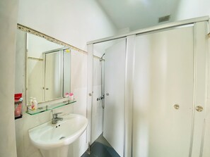 A bathroom with a white sink, a glass shelf with toiletries, a mirror, and a shower enclosure. - Bossa Nova (Da Nang)