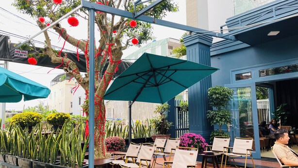 Un área de estar al aire libre con sillas y mesas, un árbol con adornos rojos y una sombrilla azul.