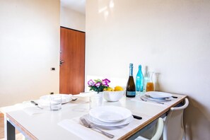 Mesa de jantar posta com pratos, copos, talheres, uma tigela de frutas e garrafas de água e vinho.