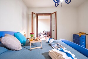 A bedroom with a bed, a bedside table with a tray of breakfast items, a chair, and a view of an outdoor seating area.