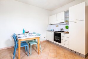 Cozinha compacta com armários brancos, fogão e pia. Há uma mesa de jantar com cadeiras e um vaso de flores.