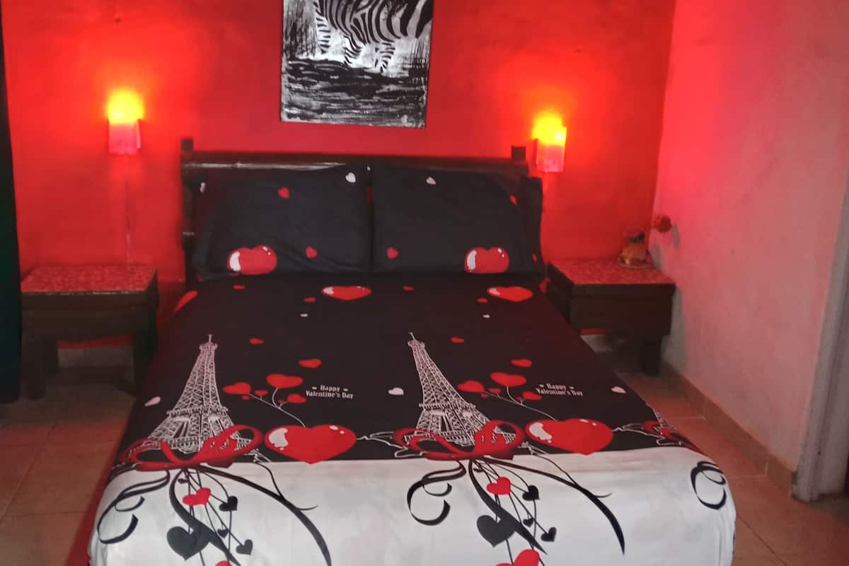 A bedroom with a bed, two bedside tables, a wall-mounted zebra painting, and red ambient lighting.