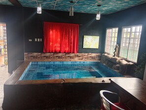 A swimming pool with a brick wall and a red curtain. There are windows with white frames and a painting on the wall.