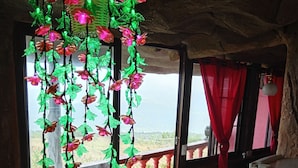 Une chambre avec vue sur un paysage montagneux, un balcon doté d’une balustrade et une décoration suspendue composée de guirlandes lumineuses et de feuilles.