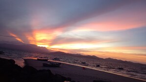 Une plage au coucher du soleil, avec des bateaux et des formations rocheuses.