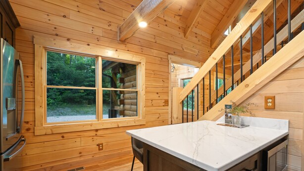 A wooden cabin interior with a large window, a kitchen counter, and a staircase. - Rustic Ravine | Hocking Hills, Hot Tub, Game Room (South Bloomingville)