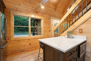 L’intérieur d’une cabane en bois, avec une grande fenêtre, un comptoir de cuisine et un escalier.