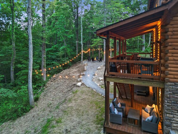 Uma cabana de toras com varanda e área de estar ao ar livre, rodeada por uma floresta.
