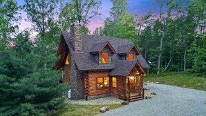 A log cabin with a stone chimney, multiple windows, and a porch. - Rustic Ravine | Hocking Hills, Hot Tub, Game Room (South Bloomingville)
