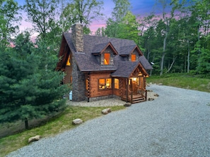 A log cabin with a stone chimney, multiple windows, and a porch.