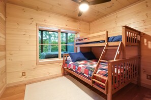 Quarto de cabana de madeira com beliche, janela e ventoinha no teto.