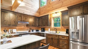 A modern kitchen with wooden cabinets, stainless steel appliances, and a large island with seating. - Rustic Ravine | Hocking Hills, Hot Tub, Game Room (South Bloomingville)