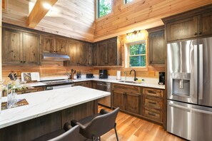 A modern kitchen with wooden cabinets, stainless steel appliances, and a large island with seating. - Rustic Ravine | Hocking Hills, Hot Tub, Game Room (South Bloomingville)