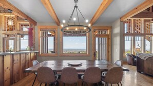 Un comedor con una gran mesa de madera, seis sillas y vistas al paisaje a través de ventanas amplias.