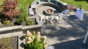 Un espacio de estar al aire libre con forma circular, que incluye un brasero rodeado de sillas tipo Adirondack y un hogar de piedra.