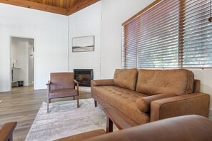 A living room with a sofa, a chair, a fireplace, and a window with blinds. - Camp Nelson Lodge Room 10 (Springville)