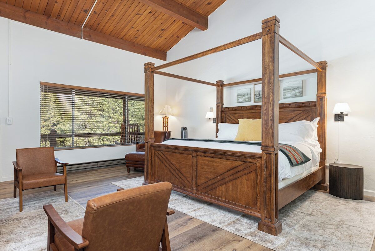 A four-poster bed with a wooden frame, two bedside lamps, and a view of greenery through a window.