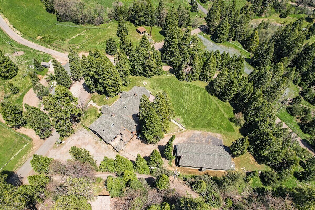 An aerial view of a residential area with a large house surrounded by dense trees and open grassy fields.