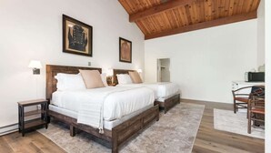 A bedroom with two beds, wooden headboards, a wooden ceiling, and a small table with a lamp.
