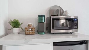 A kitchen counter with a microwave, a green water bottle, a white mug, and a small potted plant.