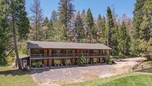 A two-story lodge with a large deck and multiple windows, surrounded by trees.