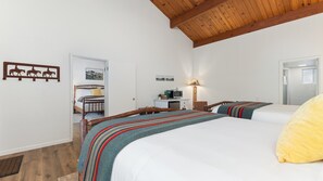 A bedroom with two beds, a wooden ceiling, a bedside table with a lamp, and a small desk with a computer. - Suite Meadow Camp Nelson Lodge# 7 (Springville)