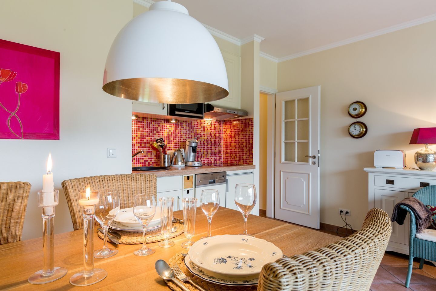 A dining area with a wooden table set for a meal, surrounded by wicker chairs.