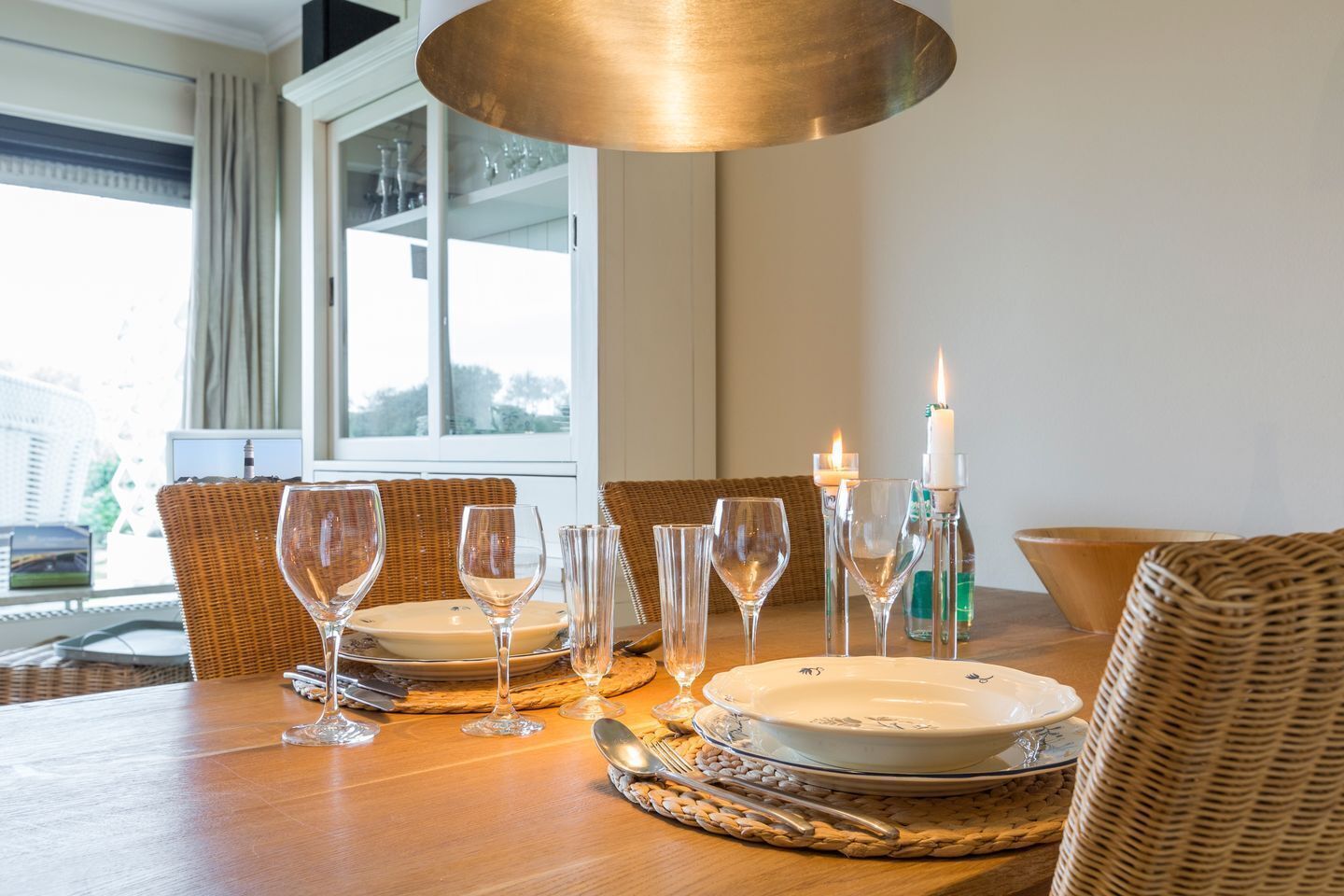 Een eettafel gedekt met borden, glazen en bestek, met een kaars en een fles op tafel.
