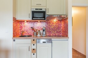 Una cocina compacta con muebles blancos, un microondas, una cafetera y un tostador.