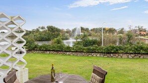 Una terrazza con tavolo, sedie, una bottiglia di vino e vista su una fontana e uno stagno.