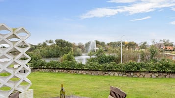 Eine Terrasse mit Tisch, Stühlen, einer Weinflasche und Blick auf einen Springbrunnen und Teich.