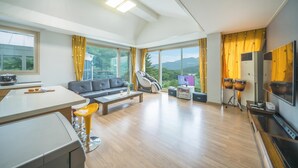 A modern living room with a sofa, a massage chair, a TV, and a kitchen area with a stove and a coffee table. - Gapyeong Yeonkkocchosu Pet Pension (Gapyeong)