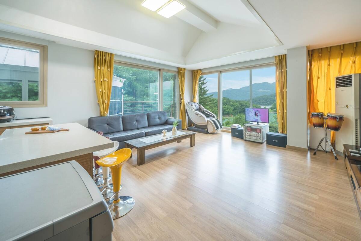 A modern living room with a sofa, a massage chair, a TV, and a kitchen area with a stove and a coffee table.